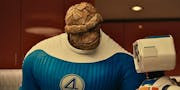 A scene from Fantastic Four: First Steps - the Thing, a rocky creature in a blue costumes, speaks to HERBIE, a small adorable robot